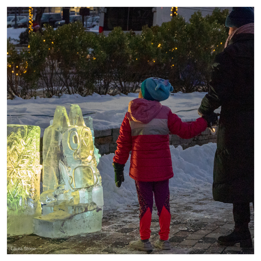 A woman holds the hand of her young daughter as they look at ice sculptures of Bluey and a snowflake